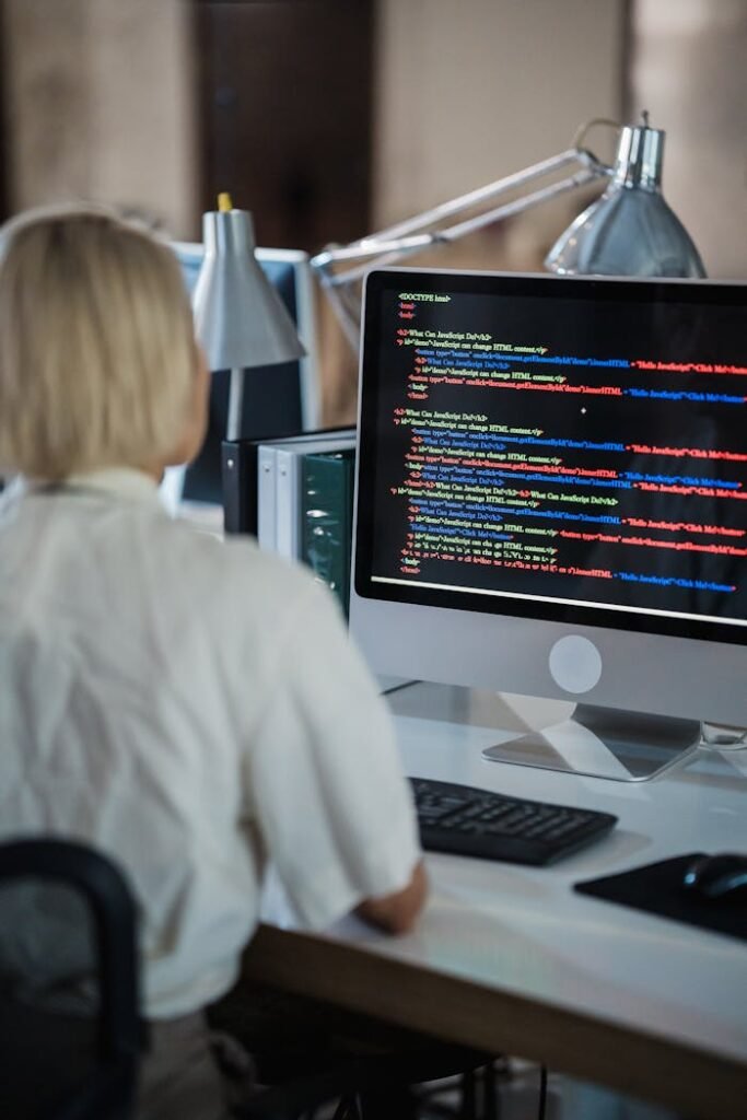 pexels photo 12899165 Professional woman coding at office desk with two monitors and desk lamps.