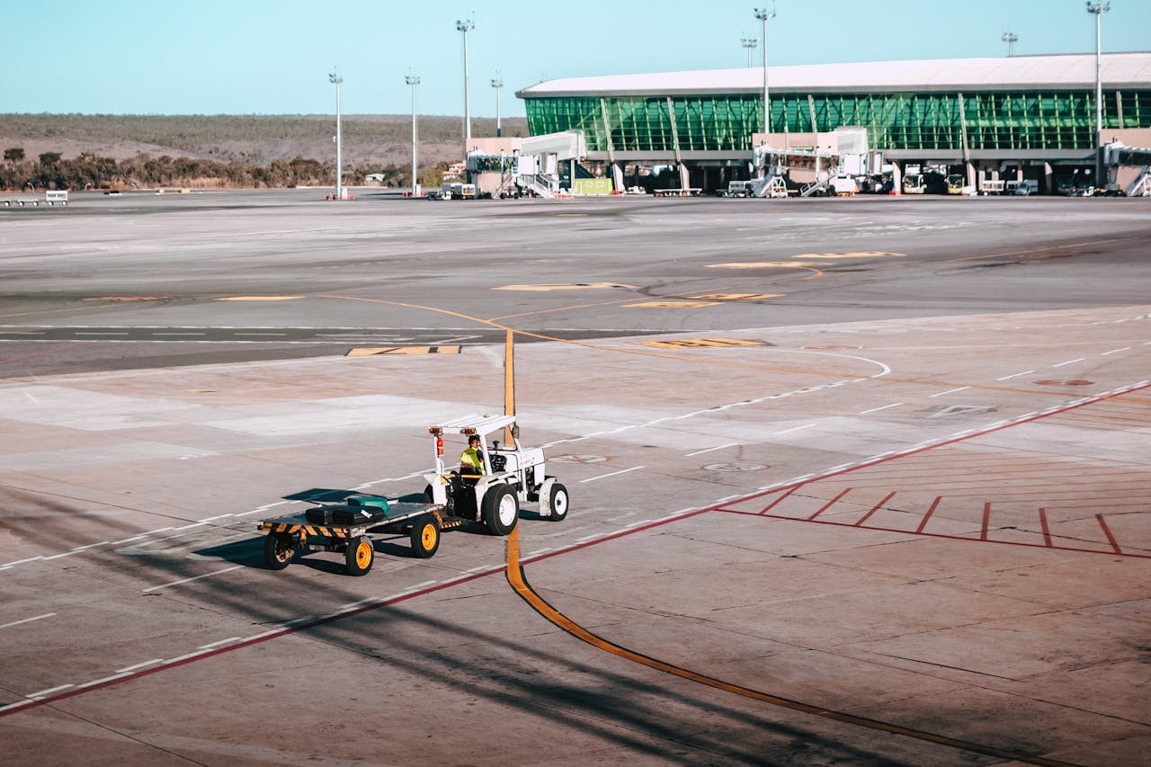 gallery-3 A luggage cart on the airport tarmac near a modern terminal building under clear skies.